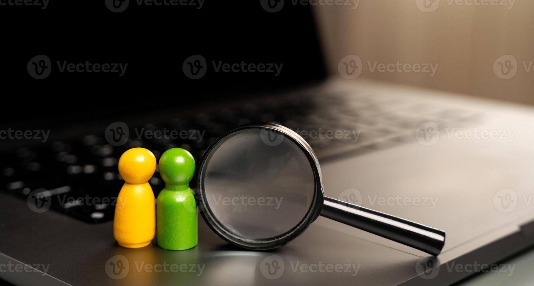 A figurine of people in the form of a pair of lovers stands on the keyboard near a magnifying glass. The concept of finding a soul mate and love online. photo