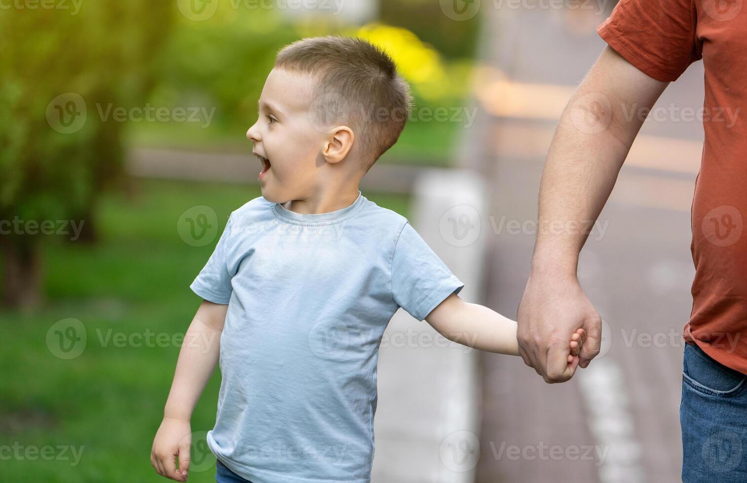 A happy three and a half years son walks hand in hand with his dad in the park on a sunny summer day. Family fun time and leisure. photo