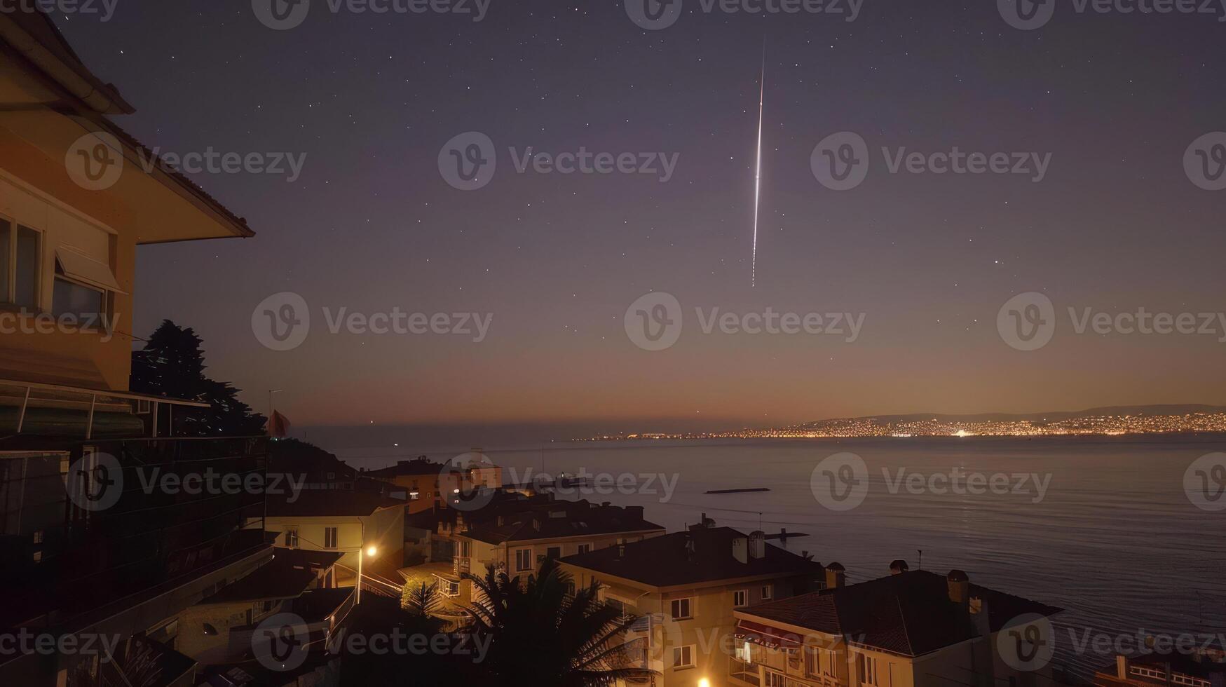 Night sky view over a coastal town with a meteor streaking across the starry sky photo