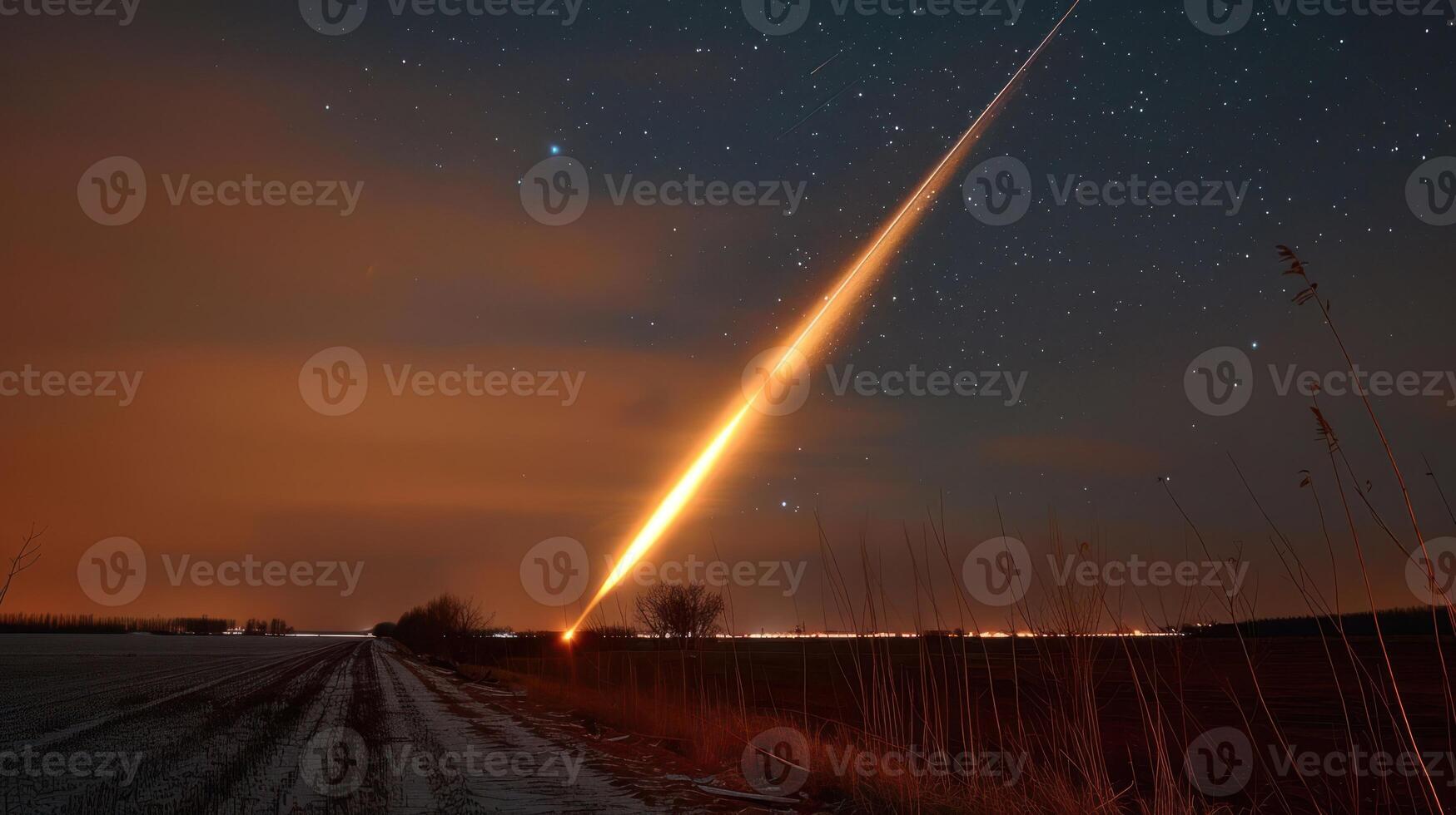 Bright meteor streaking across a starry night sky over a rural landscape with distant lights photo