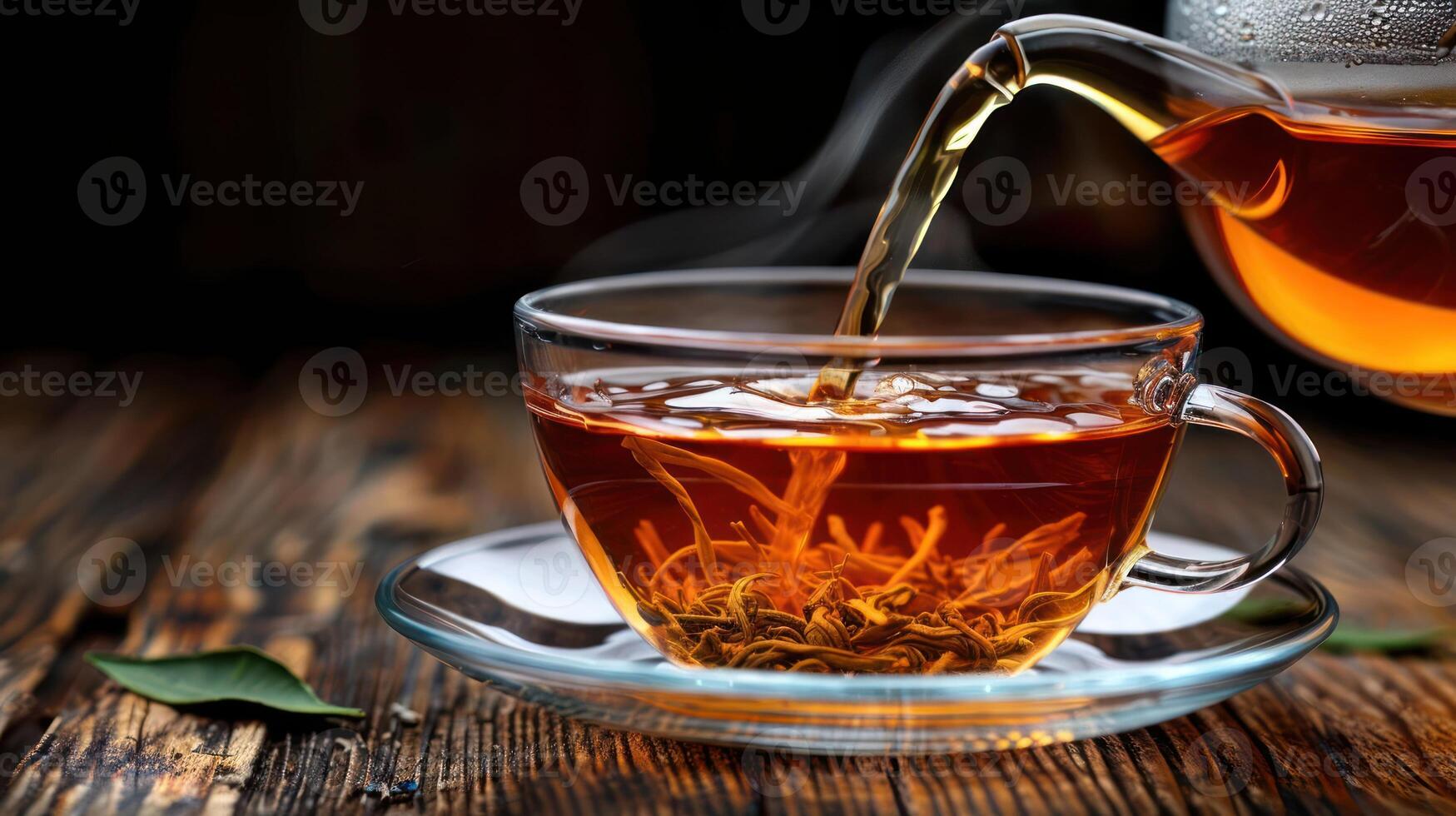 A steaming cup of tea being poured from a glass teapot on a rustic wooden table photo