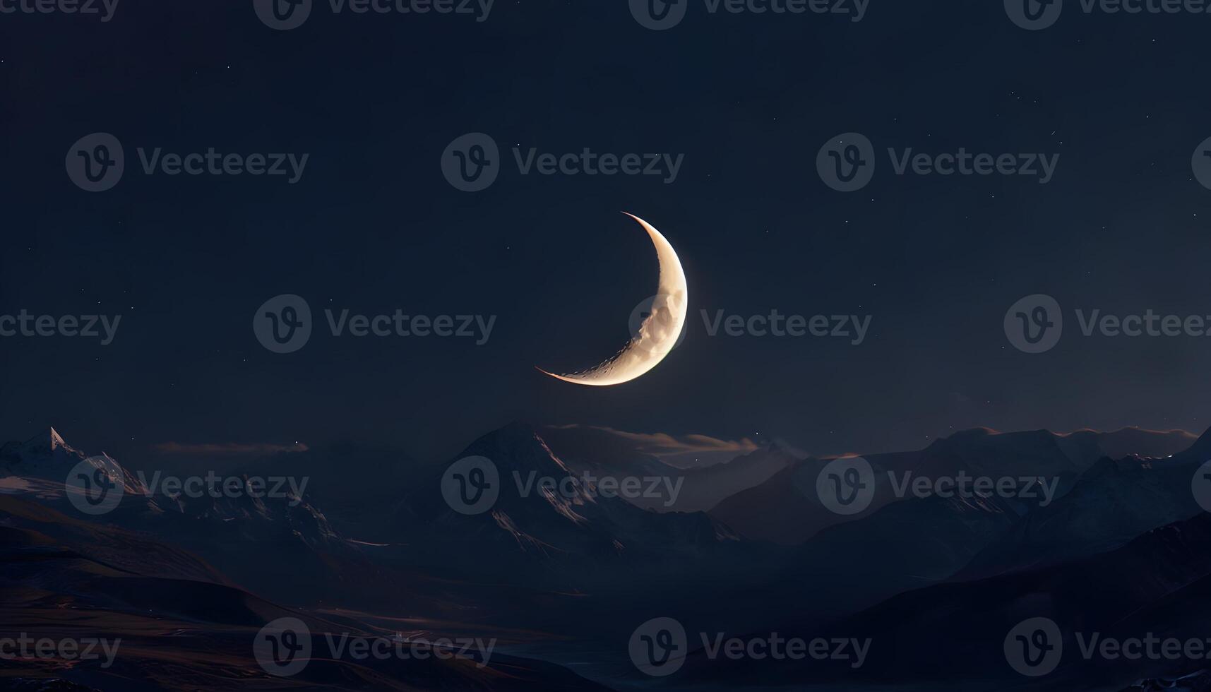 A crescent moon is seen in the night sky over mountains photo