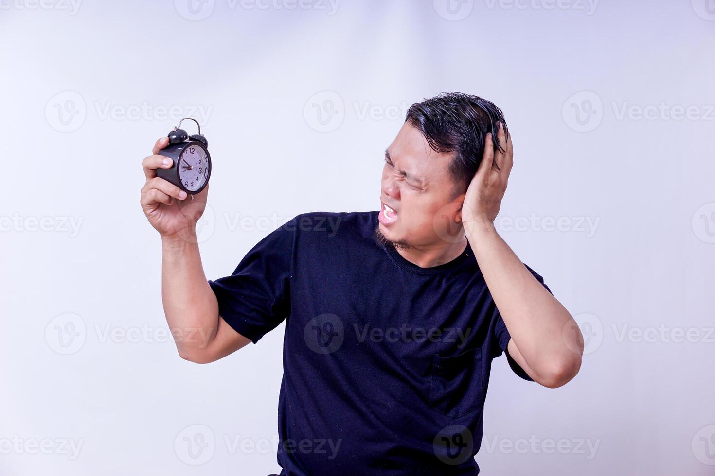An asian man shocked by the alarm clock, expressing frustration over time management isolated on white background photo