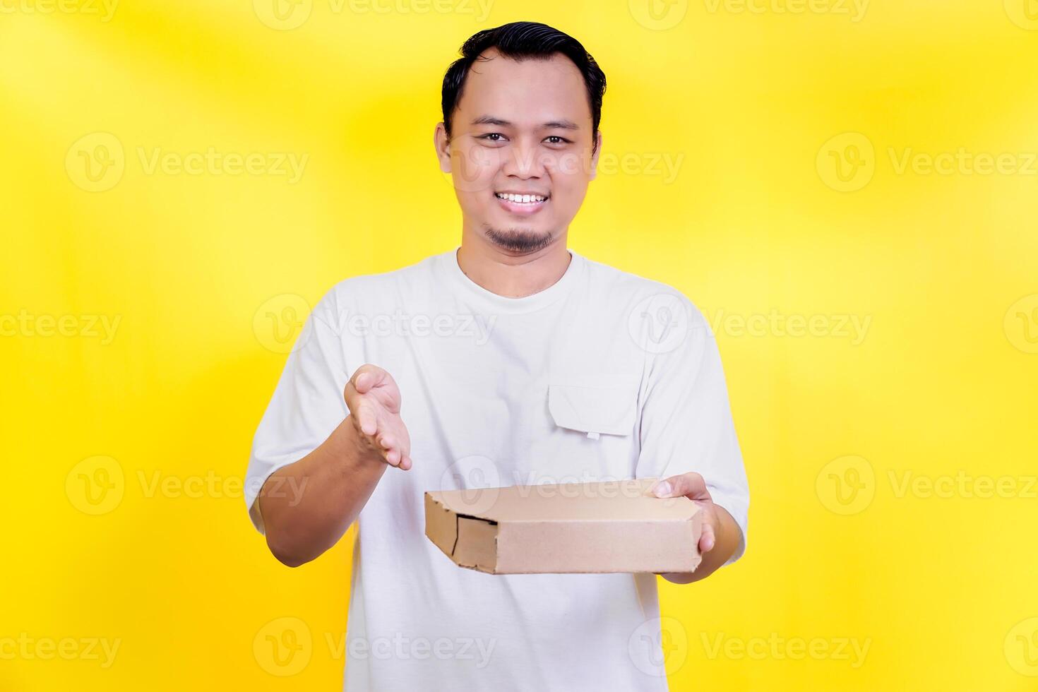 A smiling man in a white shirt holds a pizza box against a bright yellow background. international foods day concept photo