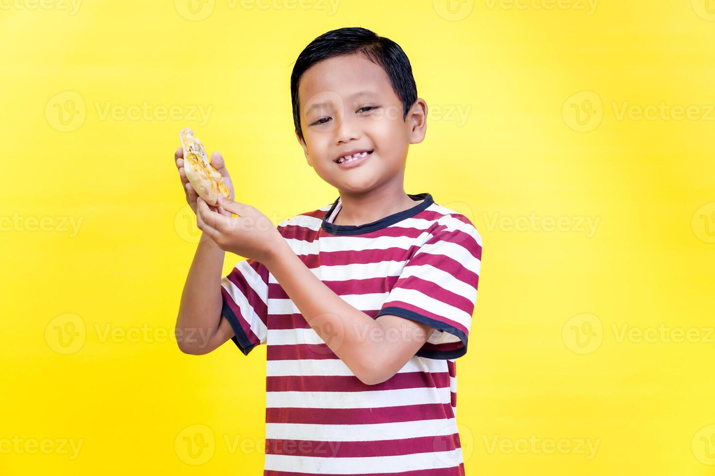A cheerful boy in a striped shirt happily holds a snack against a vibrant yellow background. international foods day concept photo
