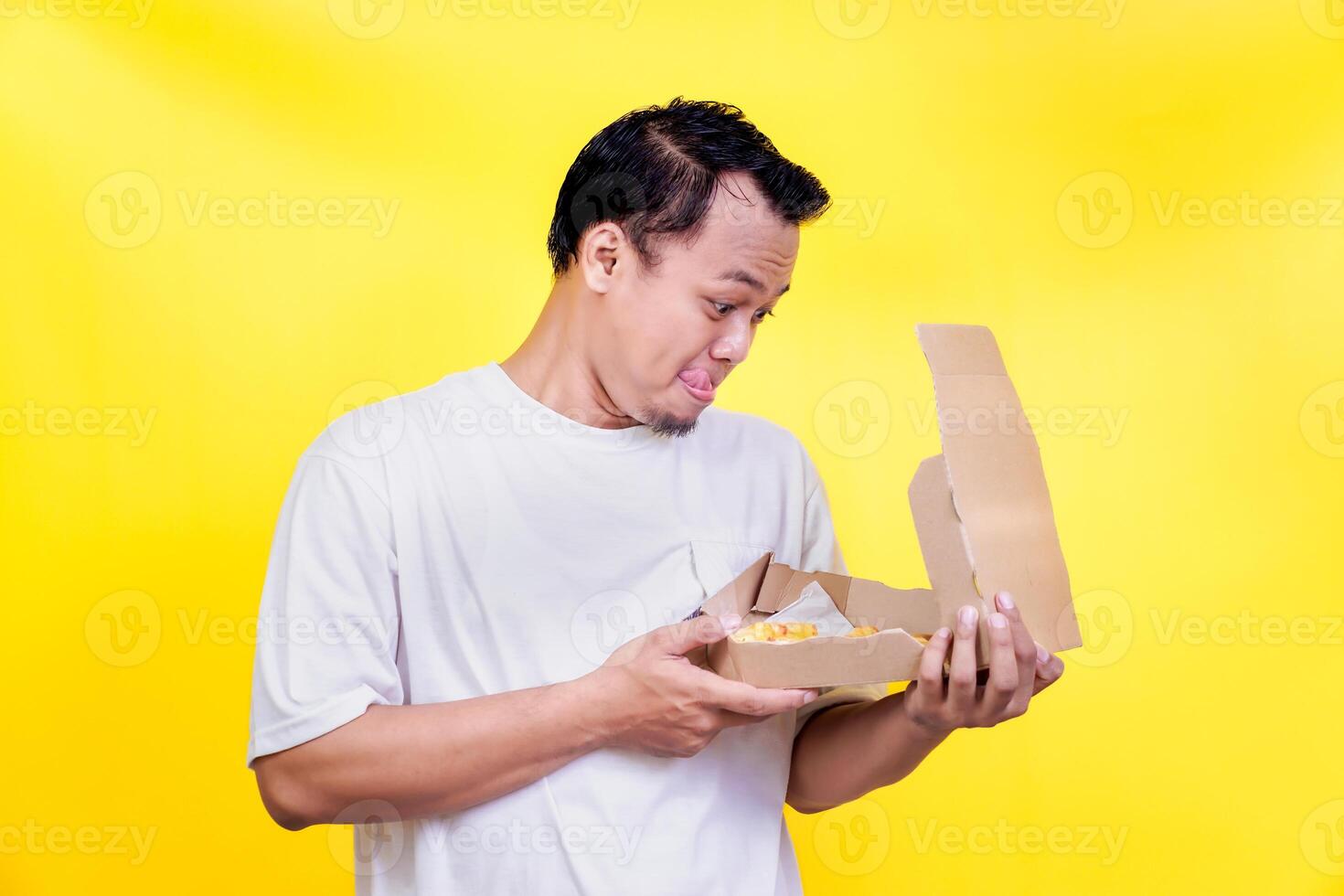 A man in a white shirt curiously examines takeout food against a vibrant yellow background. international foods day concept photo