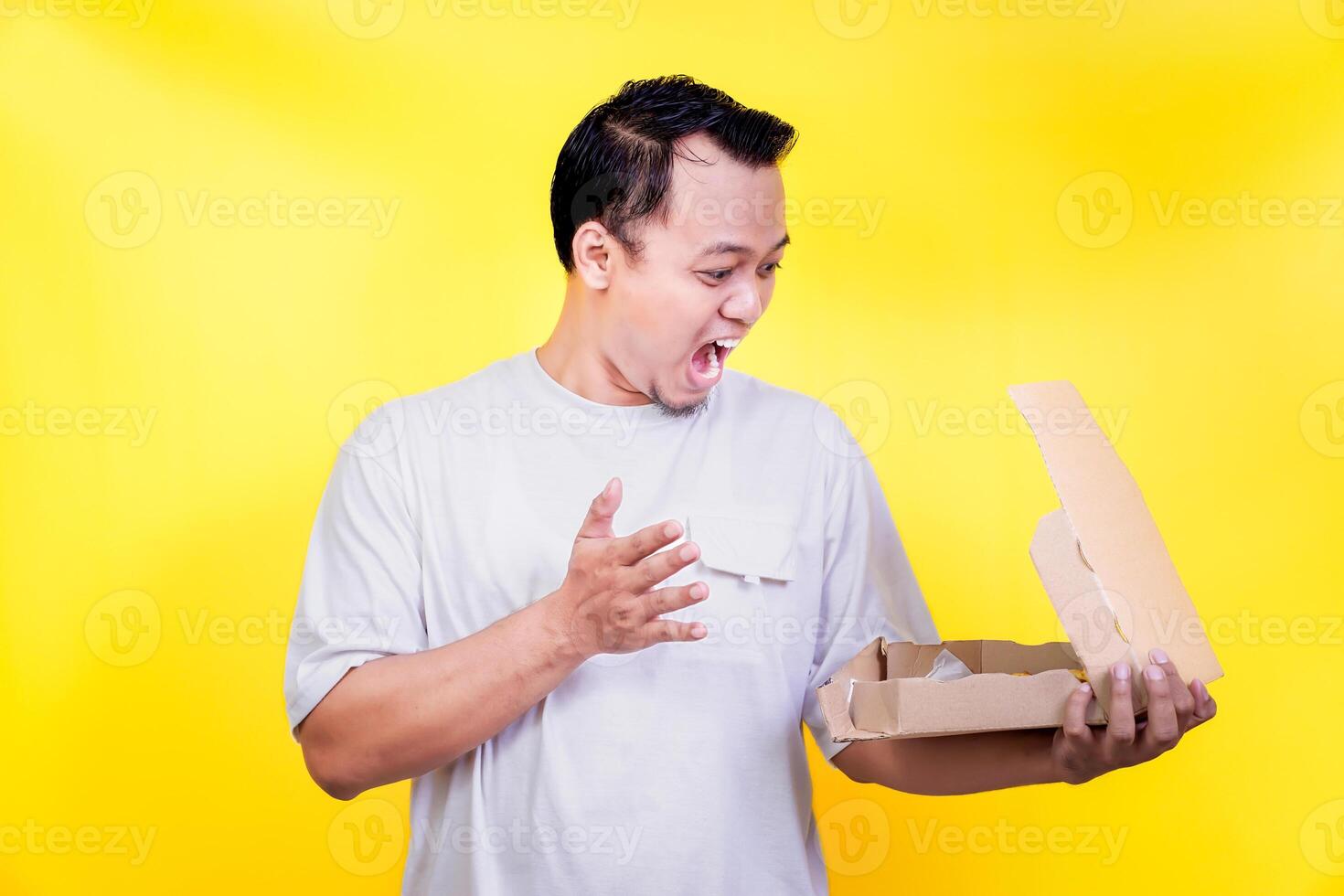 An asian surprised man opens a pizzabox, expressing excitement against a bright yellow background photo
