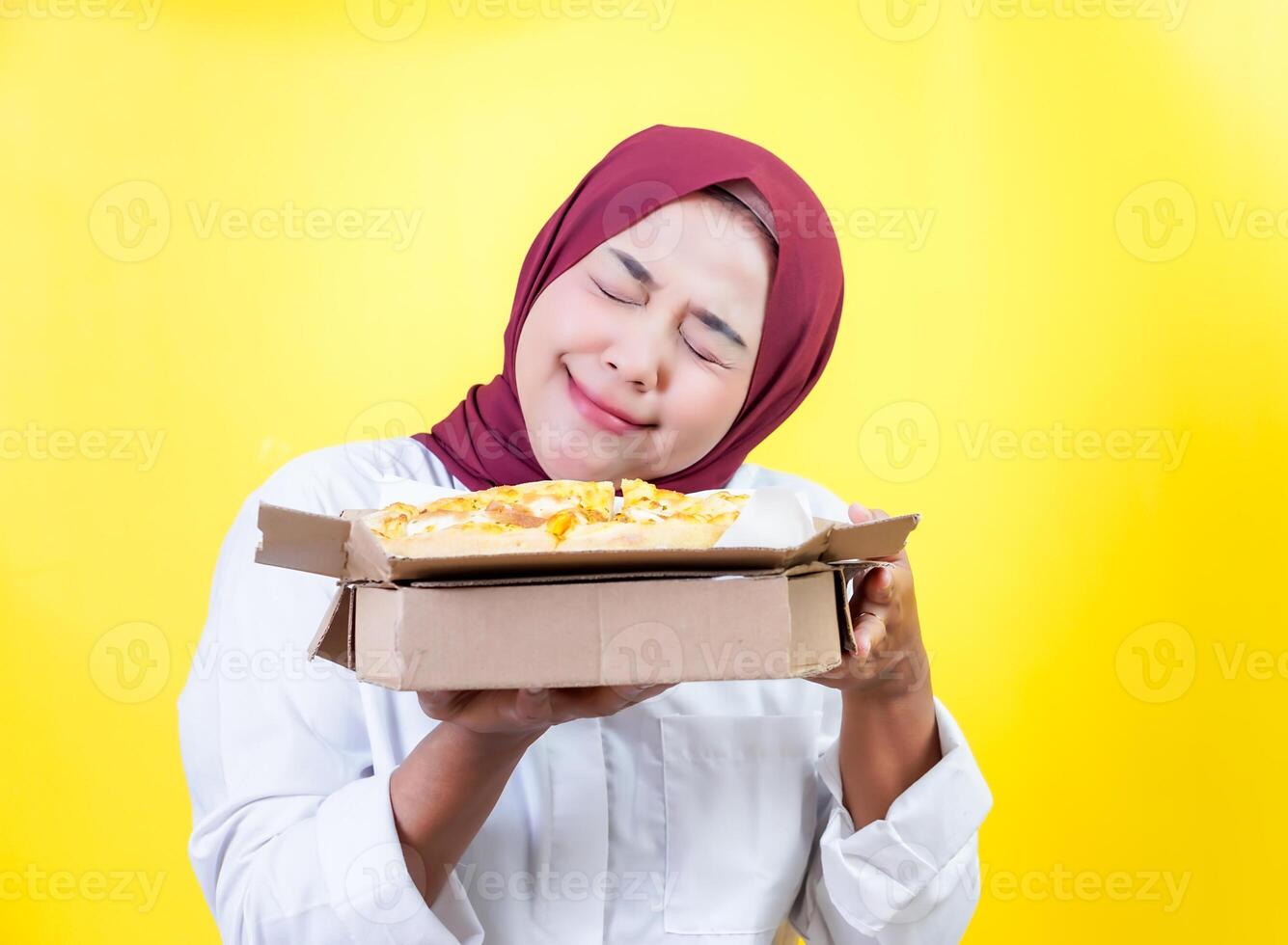 Happy asian woman in a hijab holding pizza with a playful expression photo