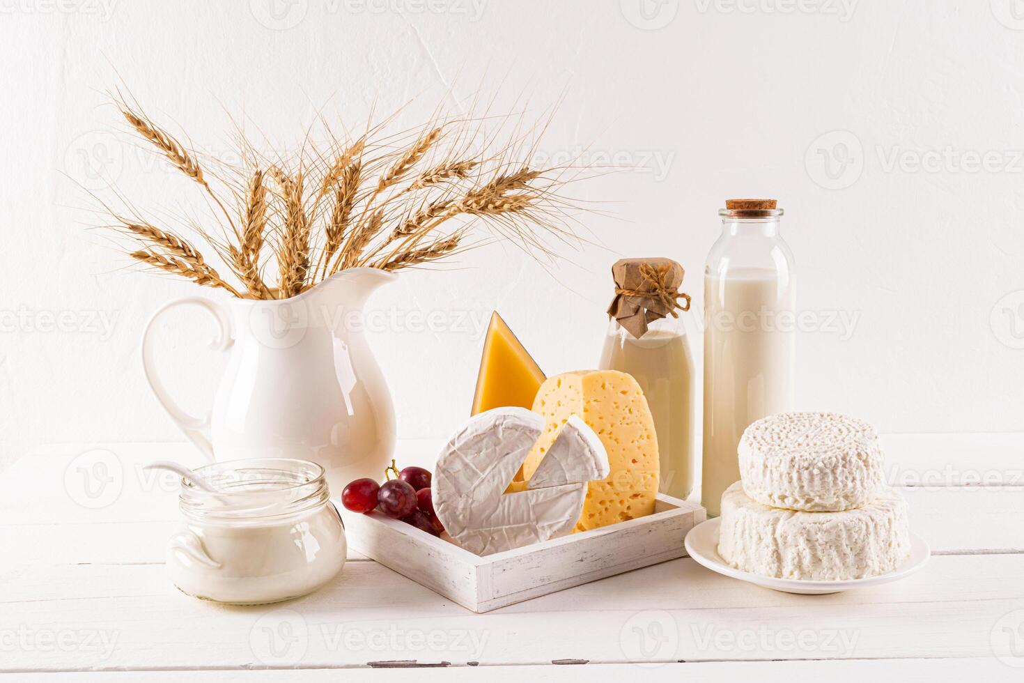 Many varieties of cheese on a board, bottles of milk, cottage cheese, sour cream, a bunch of ears of bread on a wooden table. The holiday of Shavuot. photo