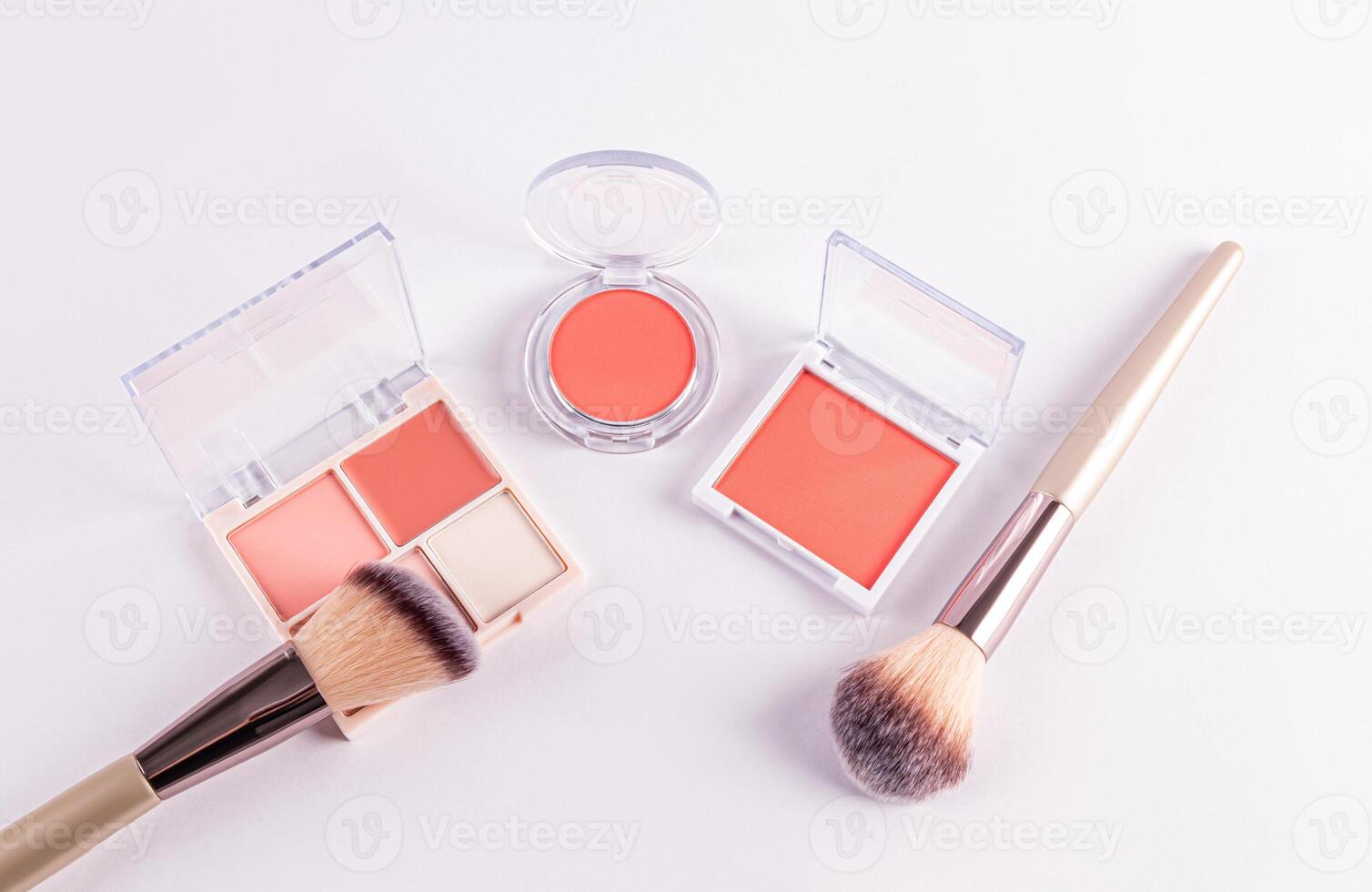 open packs with peach-tone blush and various light tones on a white background with two professional makeup brushes. top view. decorative cosmetics photo
