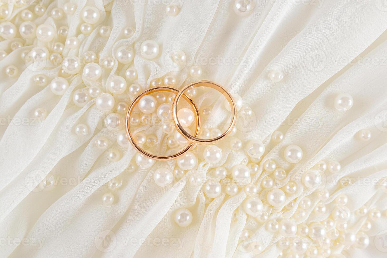 Two classic wedding gold rings lie on the drapery of chic creamy fabric with a sprinkling of pearl beads. top view. Wedding design concept. photo
