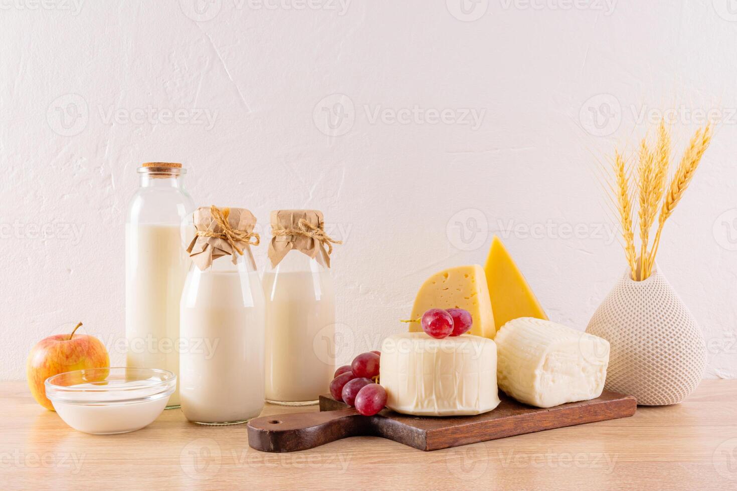 Many varieties of cheese on a board, bottles of milk, cottage cheese, sour cream, a bunch of ears of bread on a wooden table. The holiday of Shavuot photo
