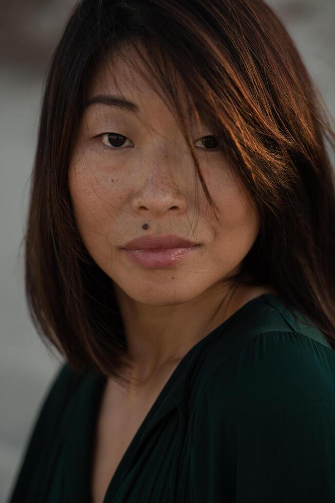 The golden hour enhances the captivating features of an Asian woman with a distinctive beauty mark. photo