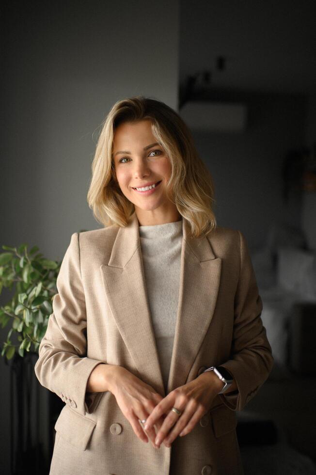 A professional blonde woman in a beige jacket looks poised and sophisticated in her business portrait. photo