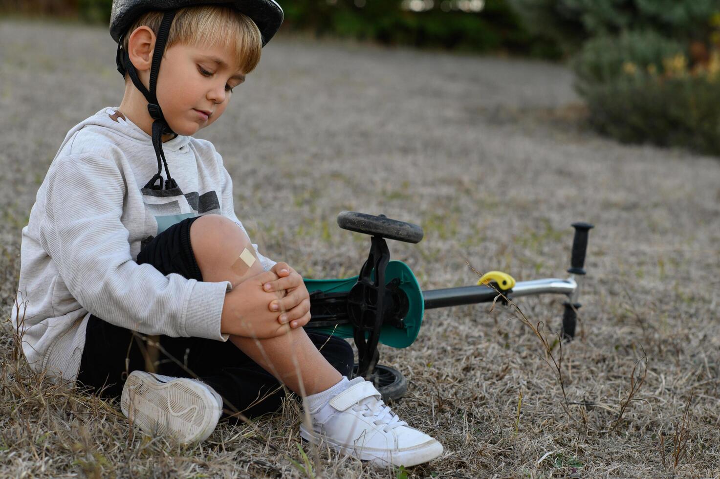 Tears in his eyes, the boy grips his knee after tumbling off his scooter. photo