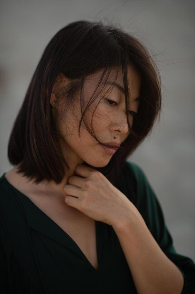 Standing on the shore, an Asian woman in a dark dress embraces the ocean breeze at dusk. photo