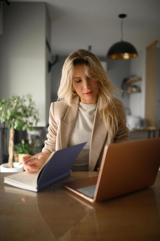 She smiles slightly as she jots down ideas in her notebook while checking her laptop screen. photo