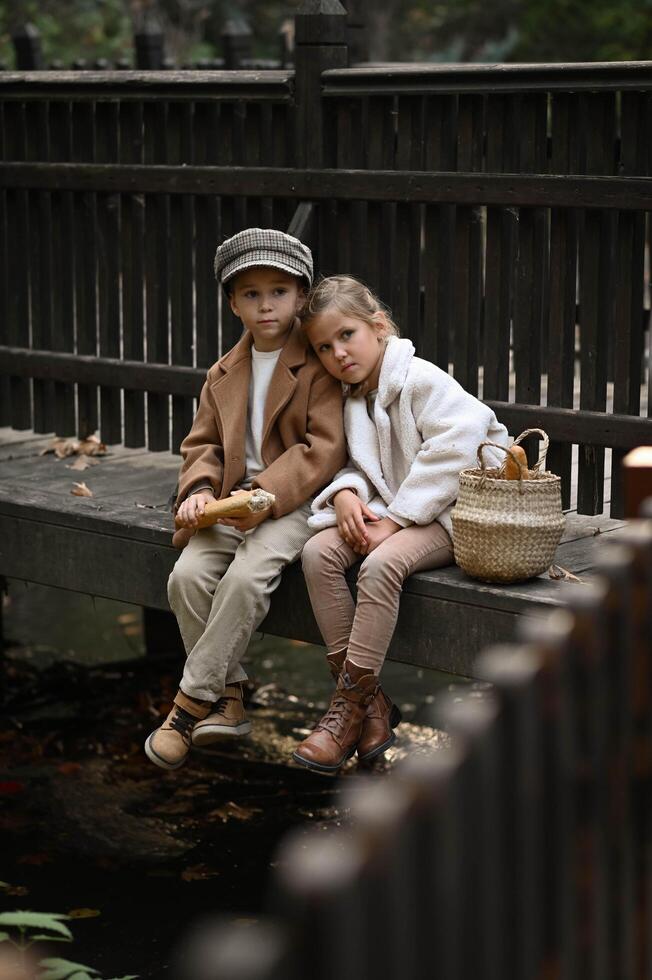 The children sit close on the wooden planks, biting into a golden baguette, their vintage-style outfits adding charm to the peaceful scene. photo