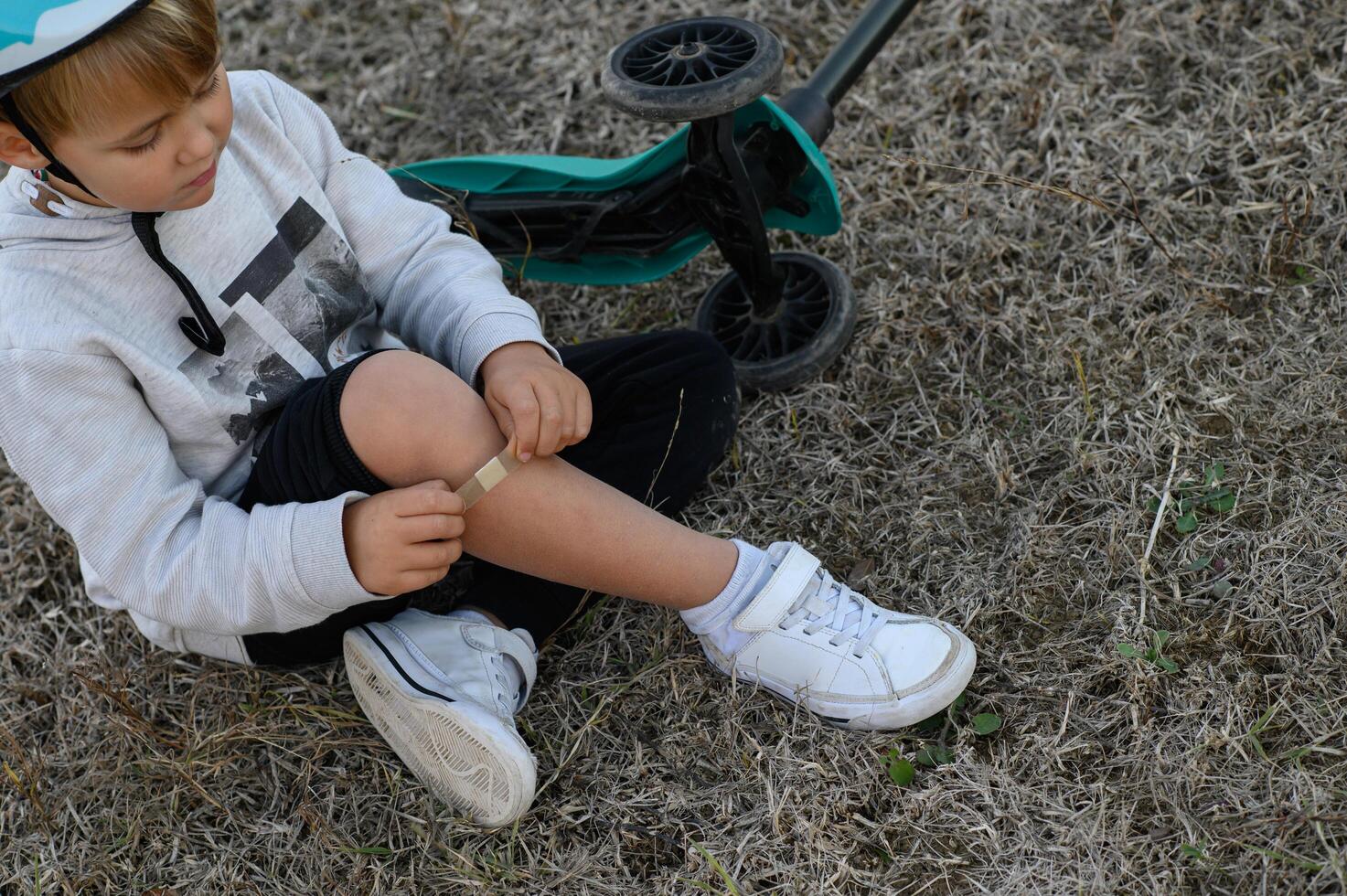 After a sudden fall, a young boy in a helmet checks his bruised knee. photo