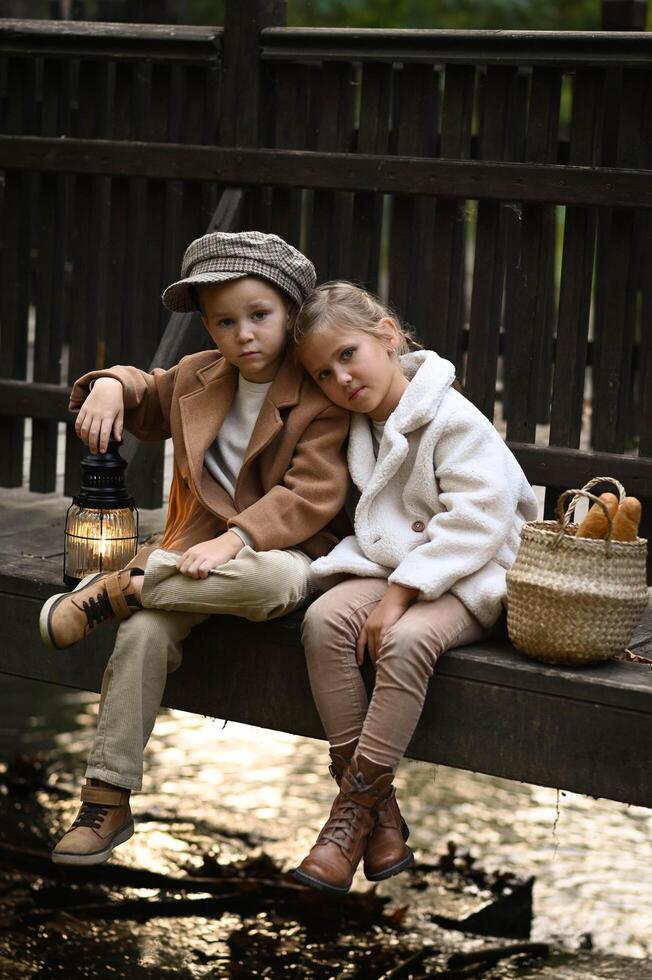 Two children sit on an old wooden bridge, sharing a fresh baguette from a wicker basket in a dreamy vintage scene. photo