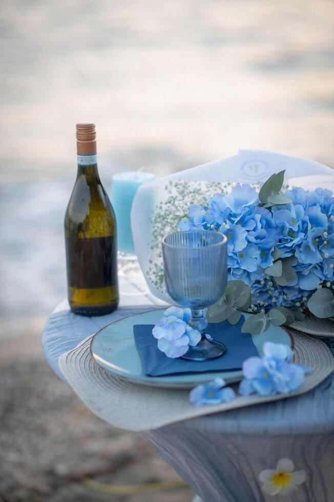 A serene table for two by the sea, bathed in the soft blue hues of twilight, as glasses of wine glisten under the fading sun. photo