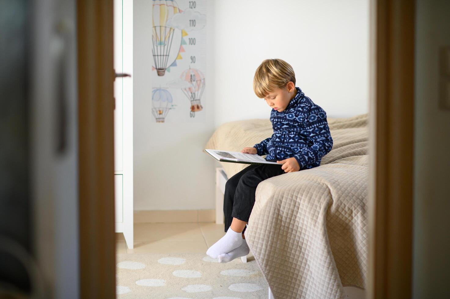 A child sits in a cozy nursery, engrossed in a book. Their eyes scan the pages with curiosity, fully absorbed in the story. photo