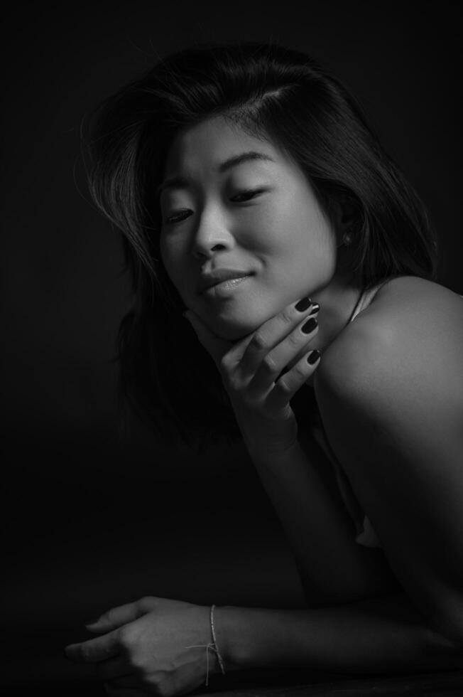 In a professional studio, an Asian woman poses elegantly, her eyes full of depth and emotion. photo