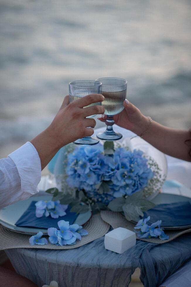The gentle waves whisper against the shore, a candlelit dinner set beneath the vast blue sky, with wine reflecting the last light of day. photo