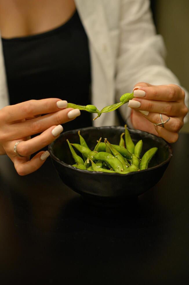 woman's hands gently pry open the fresh edamame pod, revealing the smooth green beans inside. photo