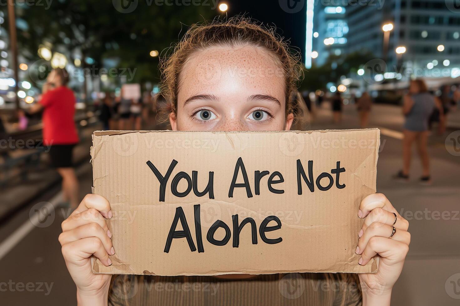 Young woman holds a cardboard sign reading You Are Not Alone at night in a city, conveying support and solidarity. Anti Bullying Day. Depression Awareness Day. World Suicide Prevention Day. photo