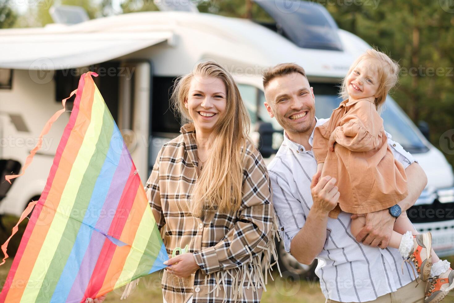 Family enjoys a sunny day outside their camper van, flying a colorful kite in a peaceful nature setting photo
