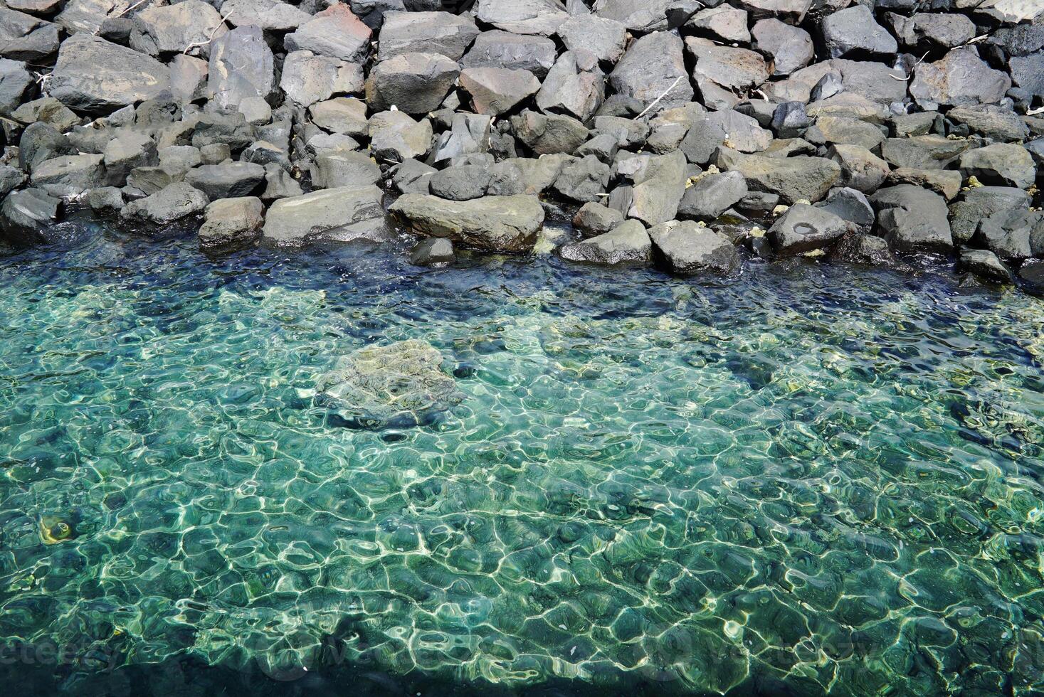 The background of the shining blue water ripples is bordered by rocks photo