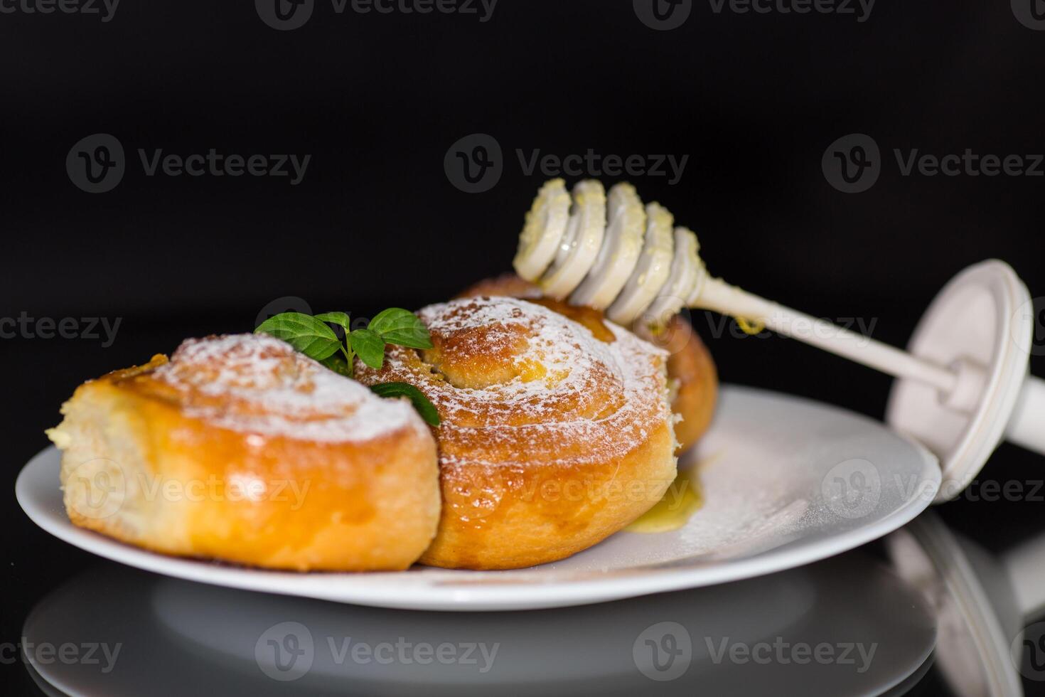 Fresh baked goods. Sweet buns with cottage cheese filling and honey in a plate isolated on a black background photo