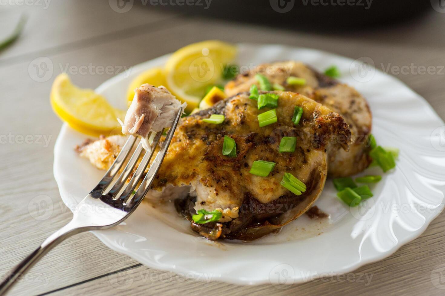 Baked fish dish with lemon and herbs in a plate on a wooden table photo