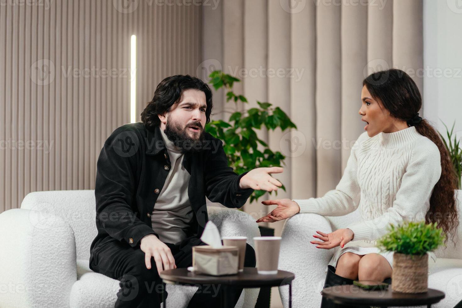 Nervous American man loses temper. Multiethnic couple having conflict during couples therapy with psychologist. African black woman argue with her husband. Psychological therapy photo
