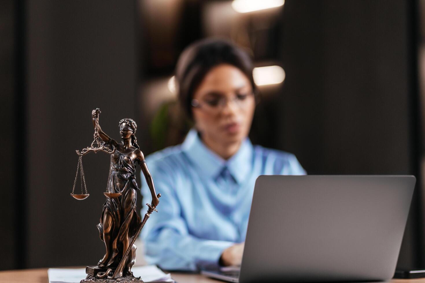 Themis, scales of justice close-up on the desk. Successful African American Attorney Lawyer using a laptop, computer in office setting. Justice and law, legal agreements concept. Blurred background photo