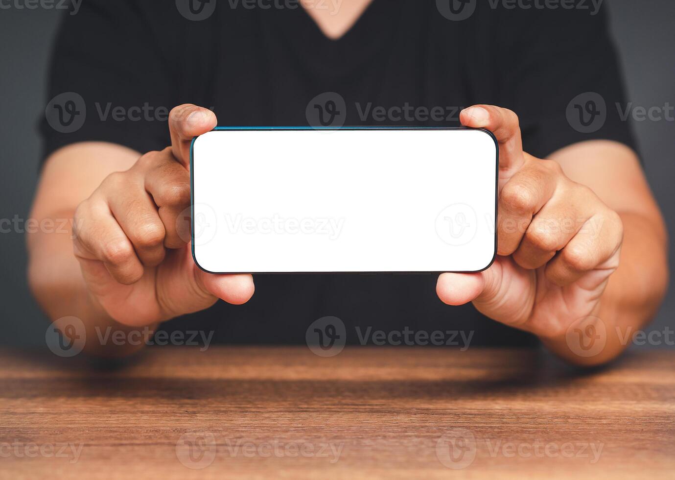 Hands of a man showing a horizontal mobile phone with a blank white screen on a wooden table photo