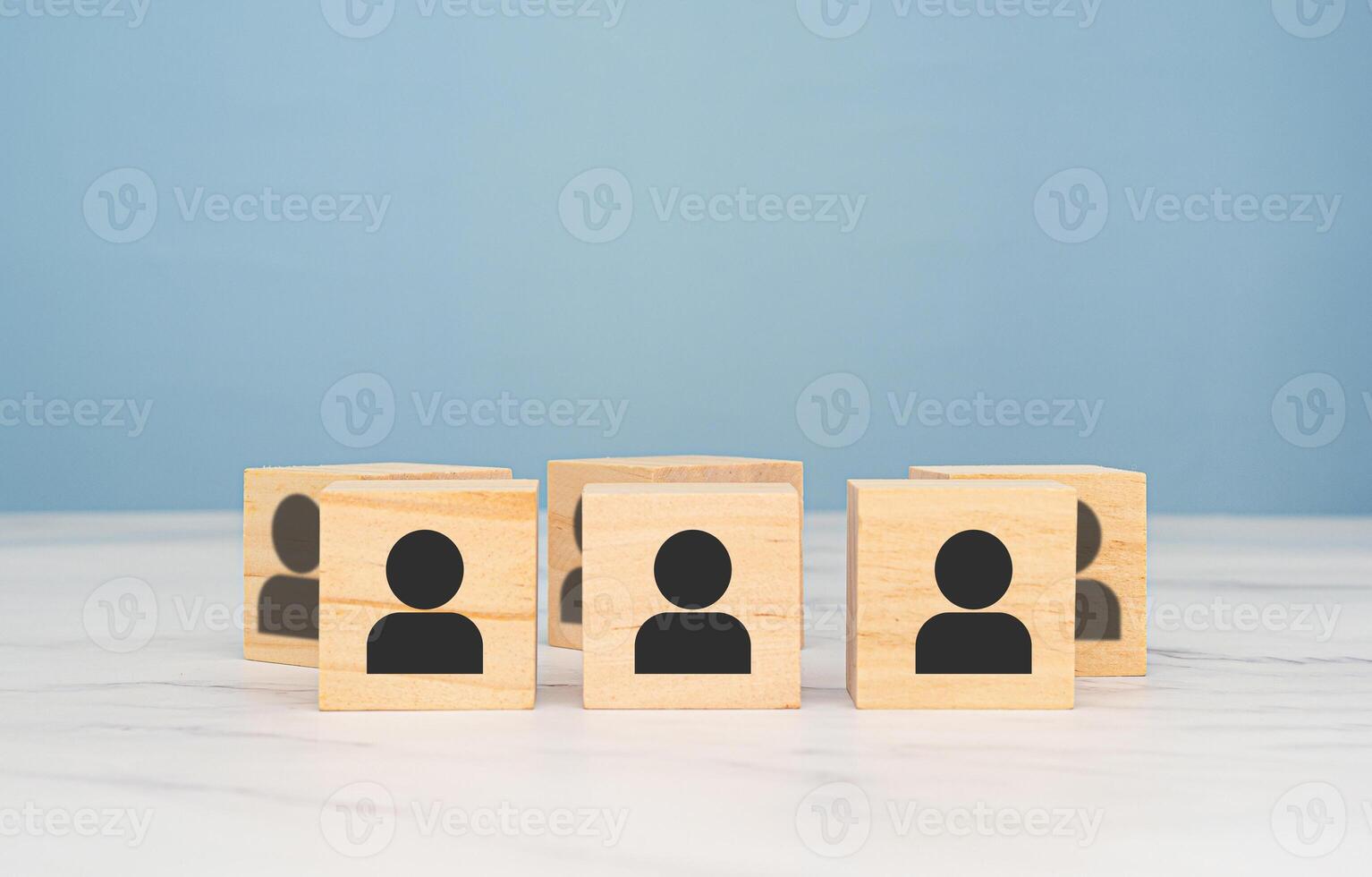 Wooden cubes with people icons over a marble table with a light blue background photo