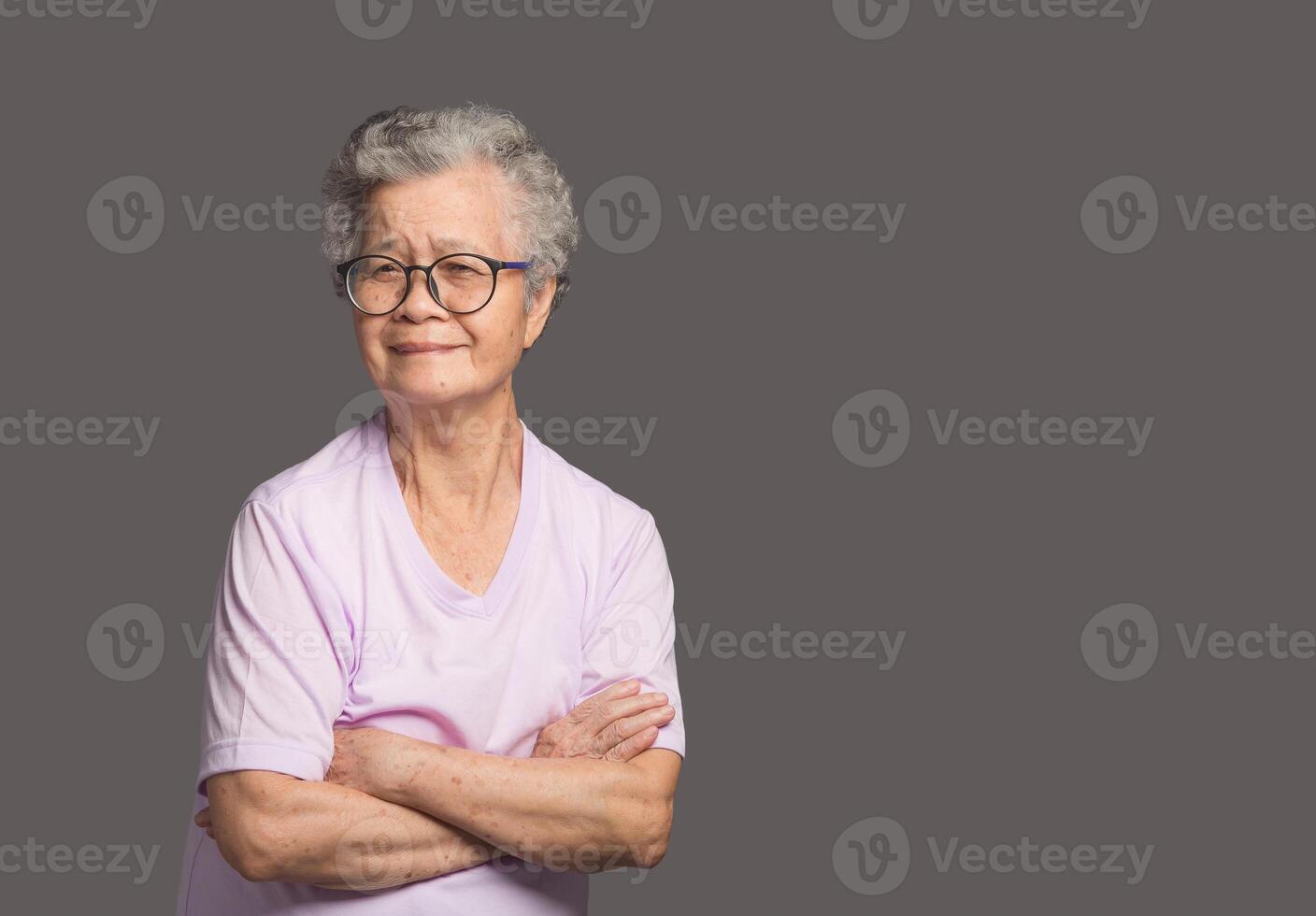 An elderly Asian woman looking at the camera with a smile while standing on a gray background photo