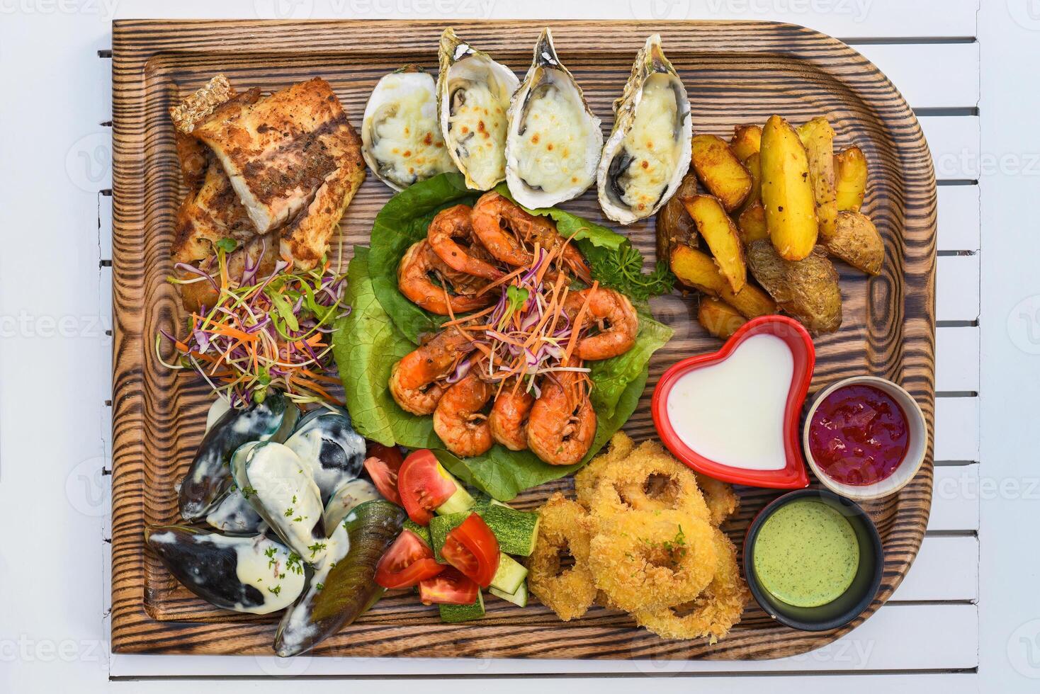 A lot of seafood as fried fish, calamari, oysters and sauces on wooden board on the table photo