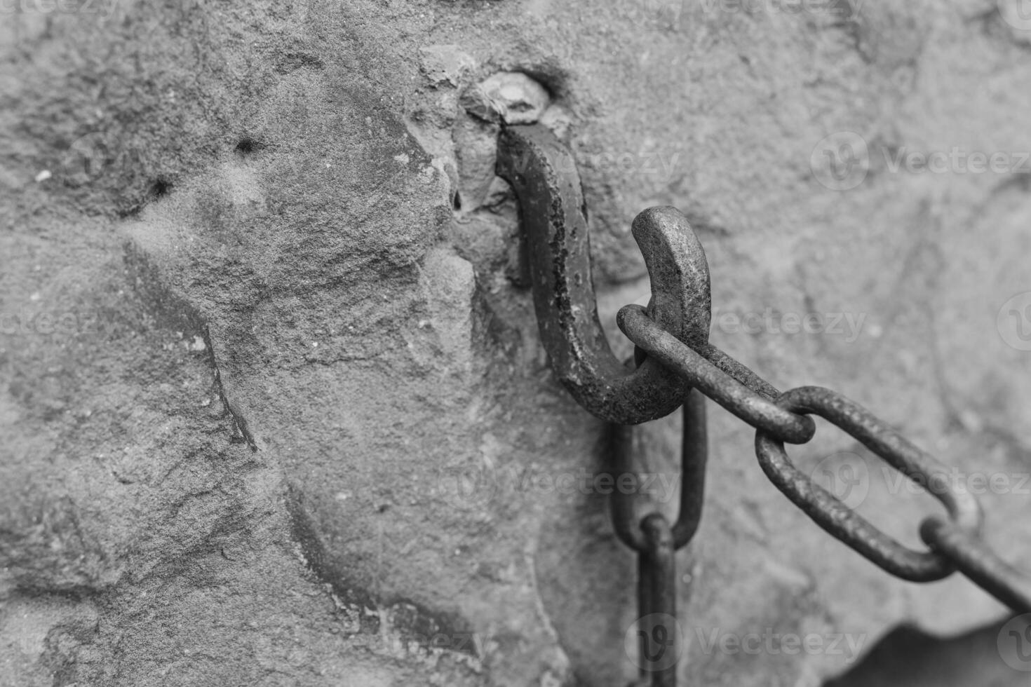 Rusty chain hook attached to a weathered stone wall in an old structure showcasing historical craftsmanship in grayscale photo