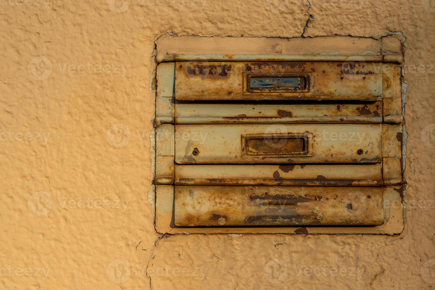 Weathered mailboxes attached to a textured wall in a quiet urban setting during late afternoon light photo