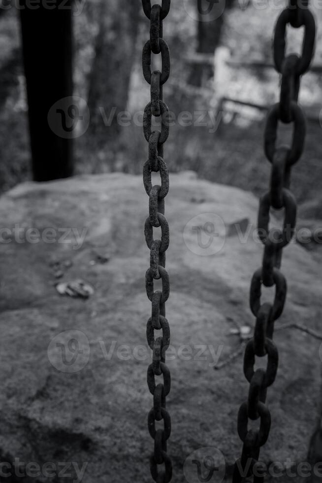 Chains hanging from a structure near a rocky area in a forest setting during a calm afternoon photo