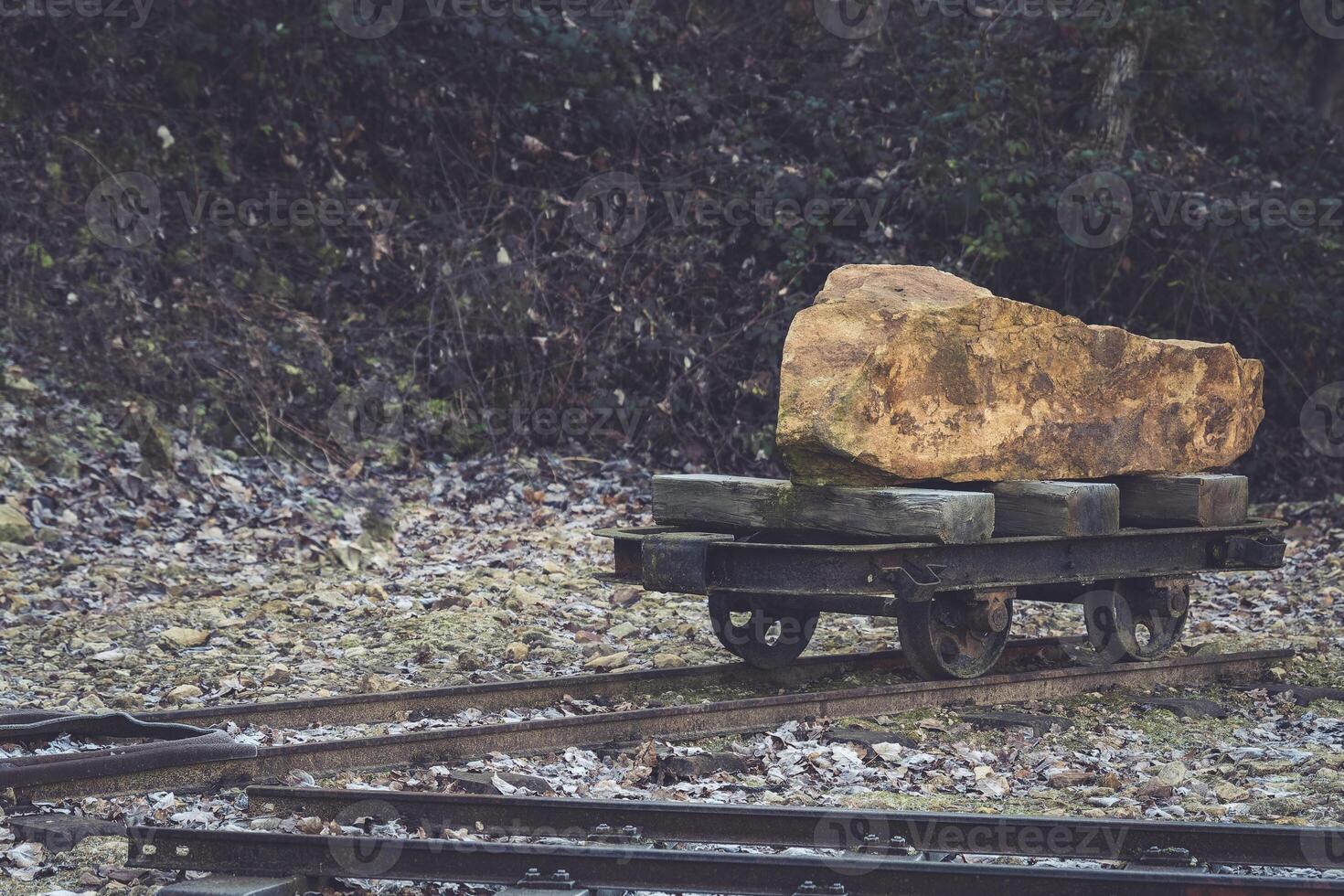 Heavy stone block on a wooden cart along old railway tracks in a forest clearing during daylight photo