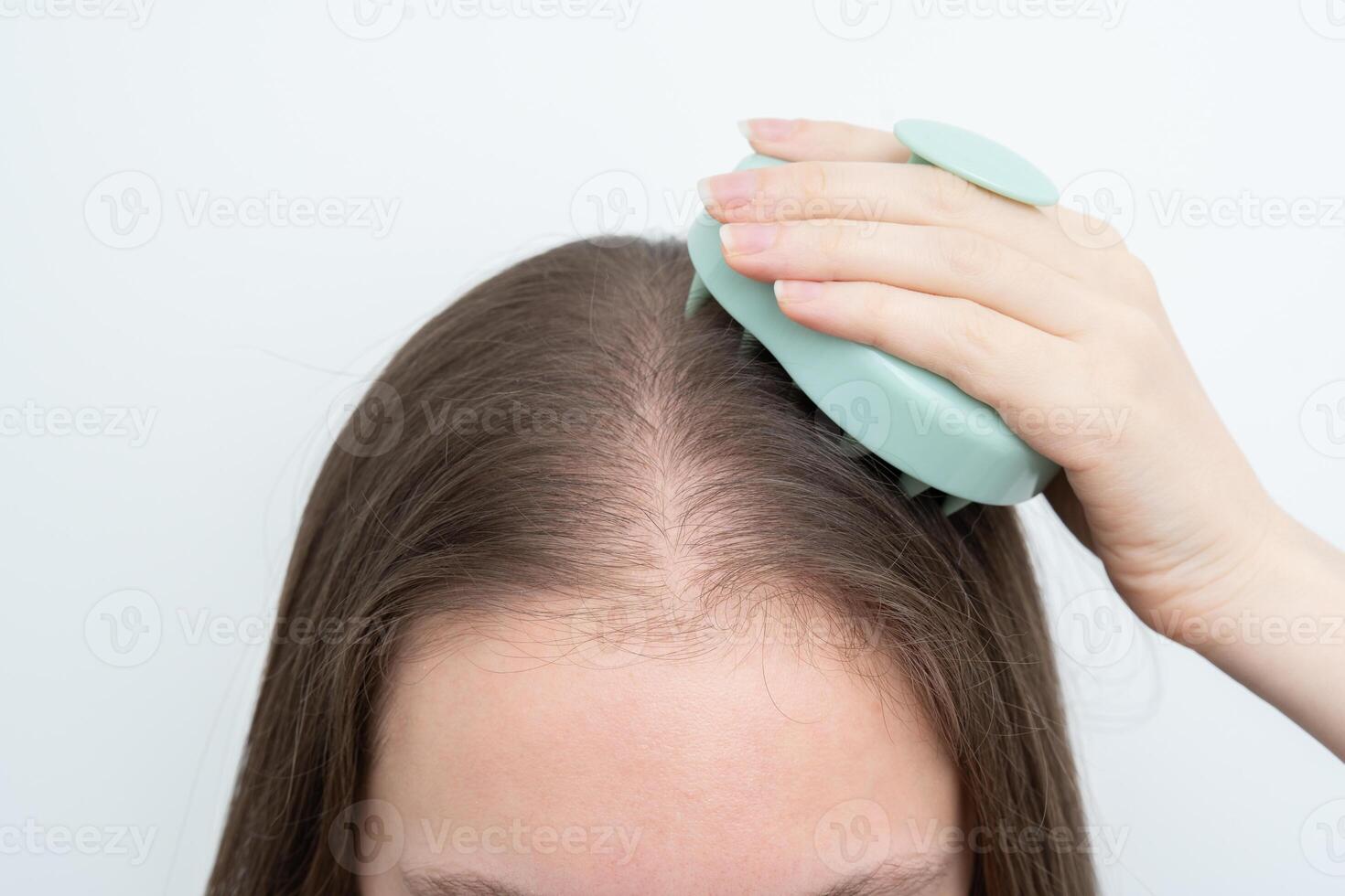 Woman using a scalp massager to stimulate hair growth and care for scalp with copy space. Concept of beauty treatment, wellness, and addressing alopecia and thinning hair through daily routines. photo