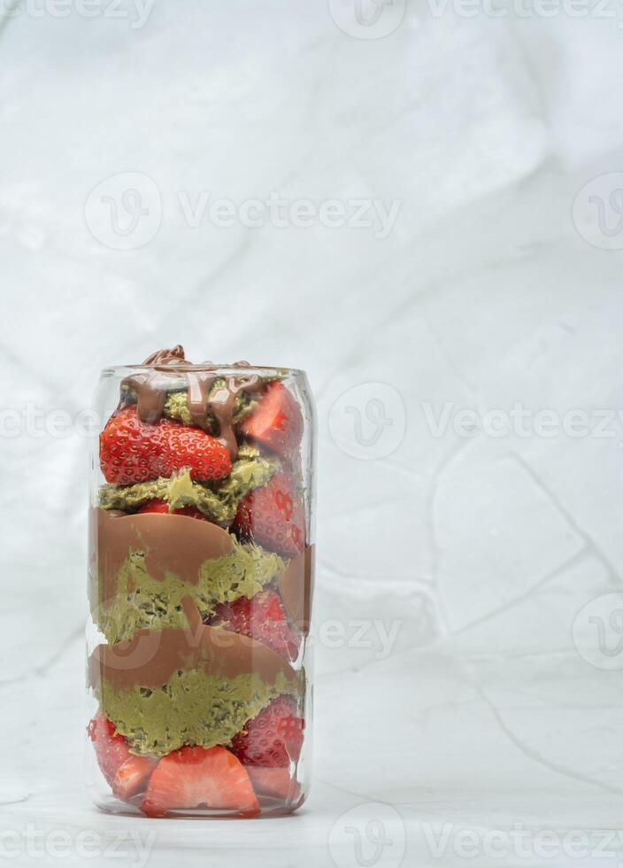 Dubai chocolate strawberry cup with kataifi, pistachio paste, tahini, milk chocolate and fresh strawberries. Vertical photo. Copy space for text. Tasty desserts and sweets, takeaway. photo
