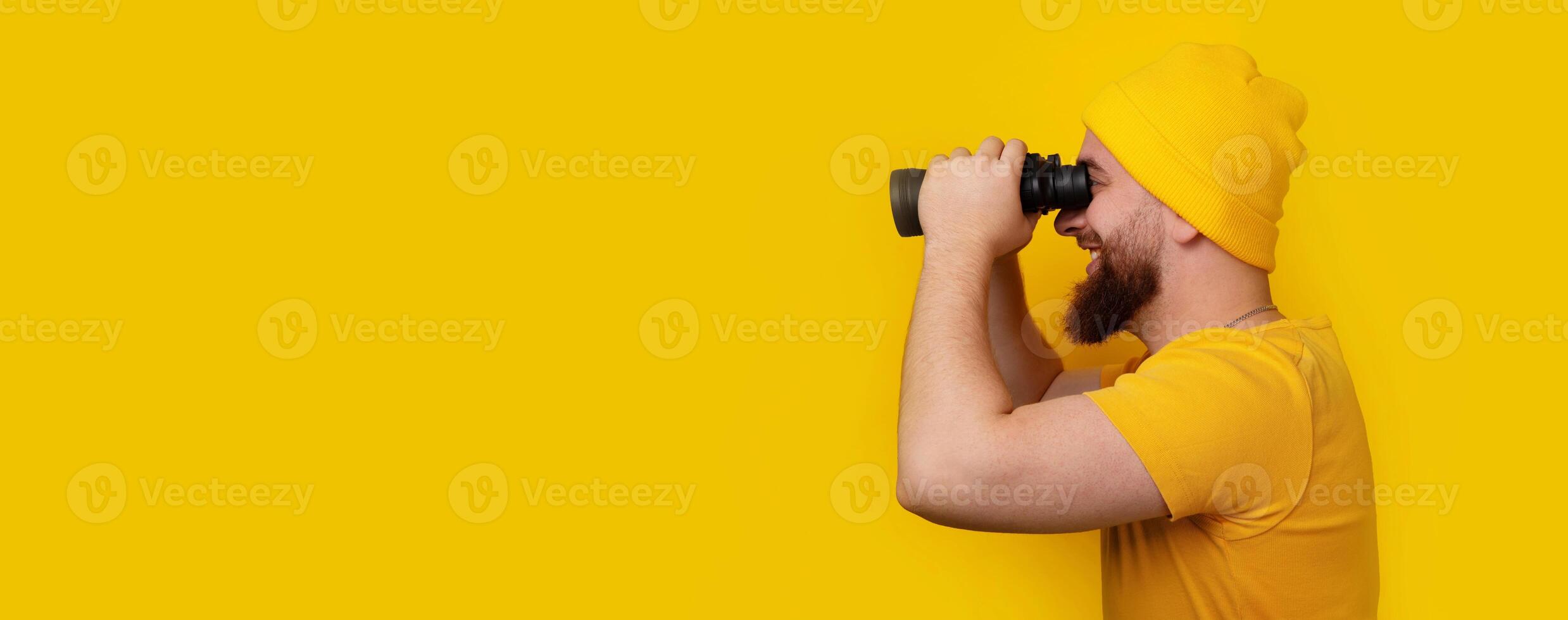 man standing in profile and looking into binoculars on yellow photo