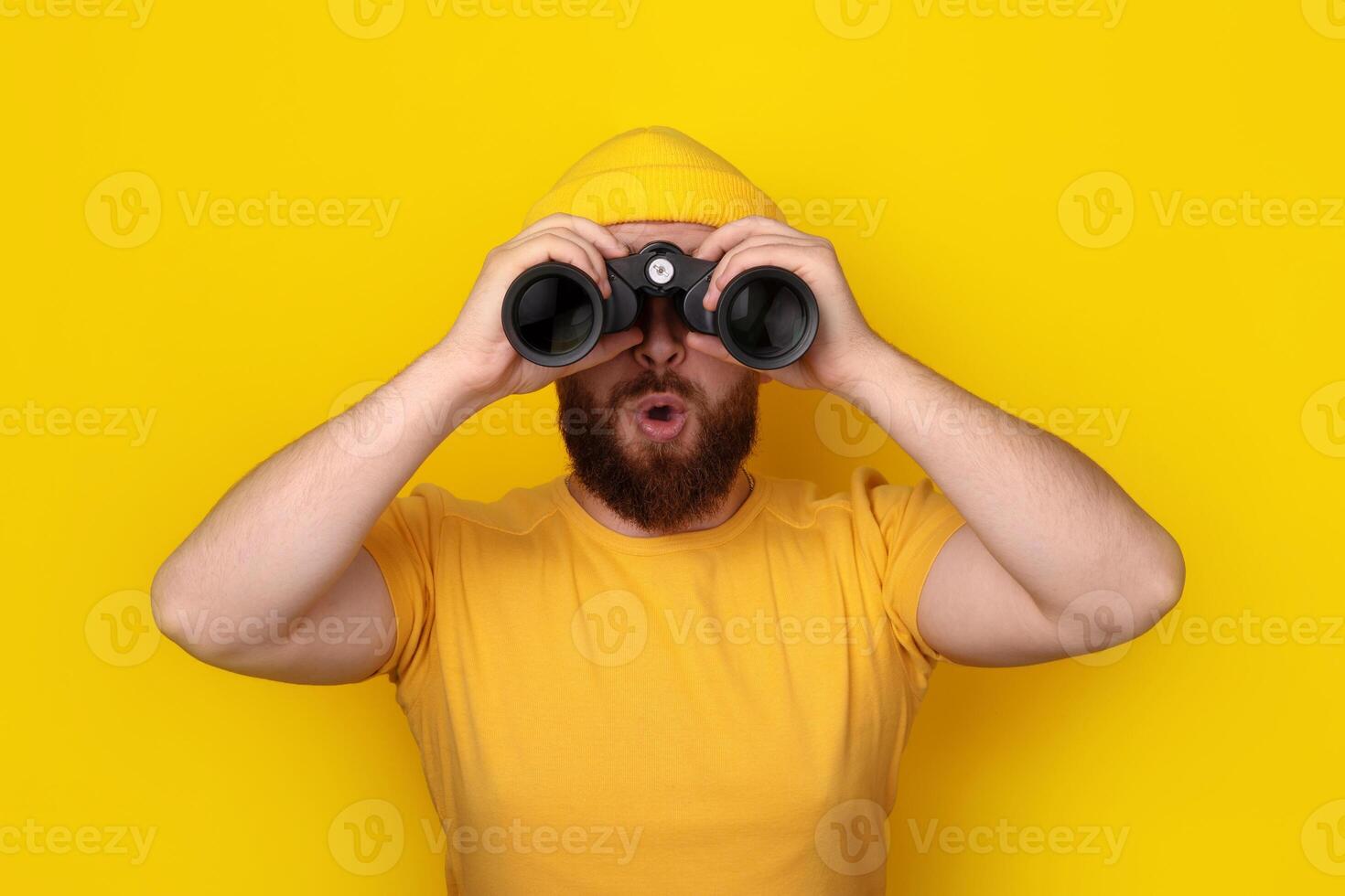 surprised man looking into binoculars on yellow photo