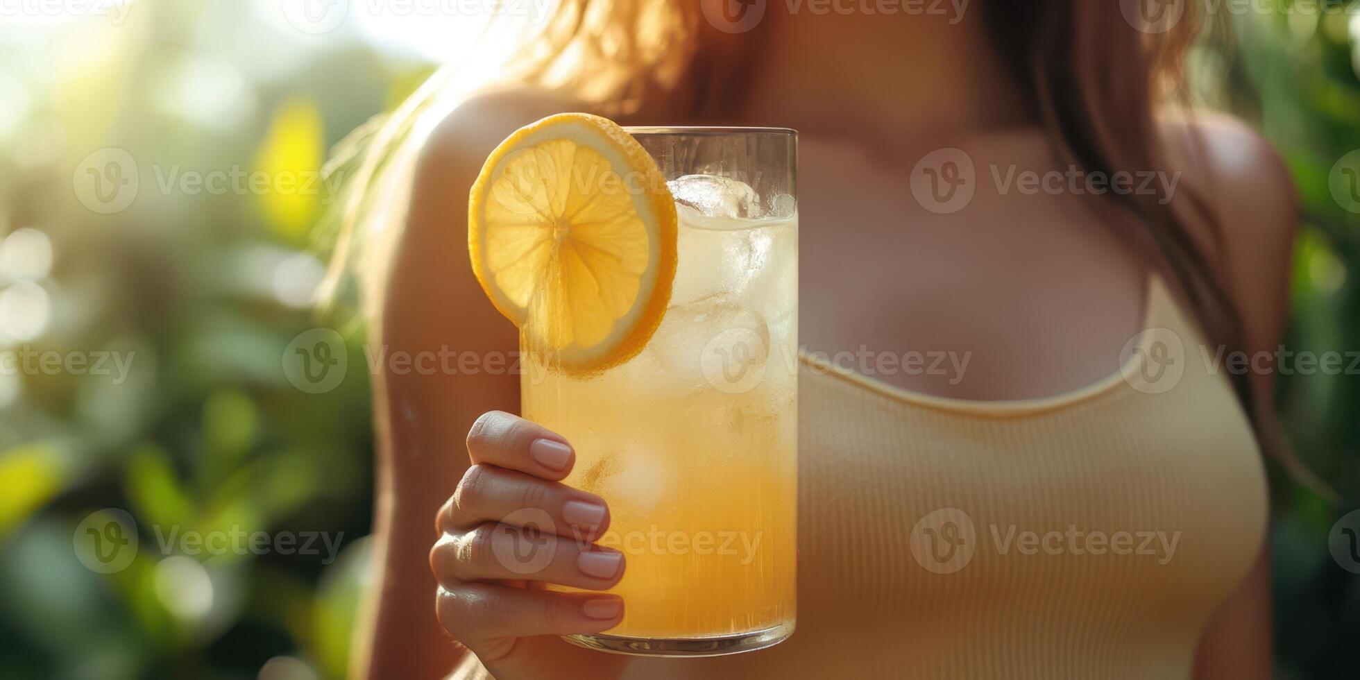 Beautiful woman enjoying a refreshing drink with lemon garnish in a sunny garden setting during late afternoon photo