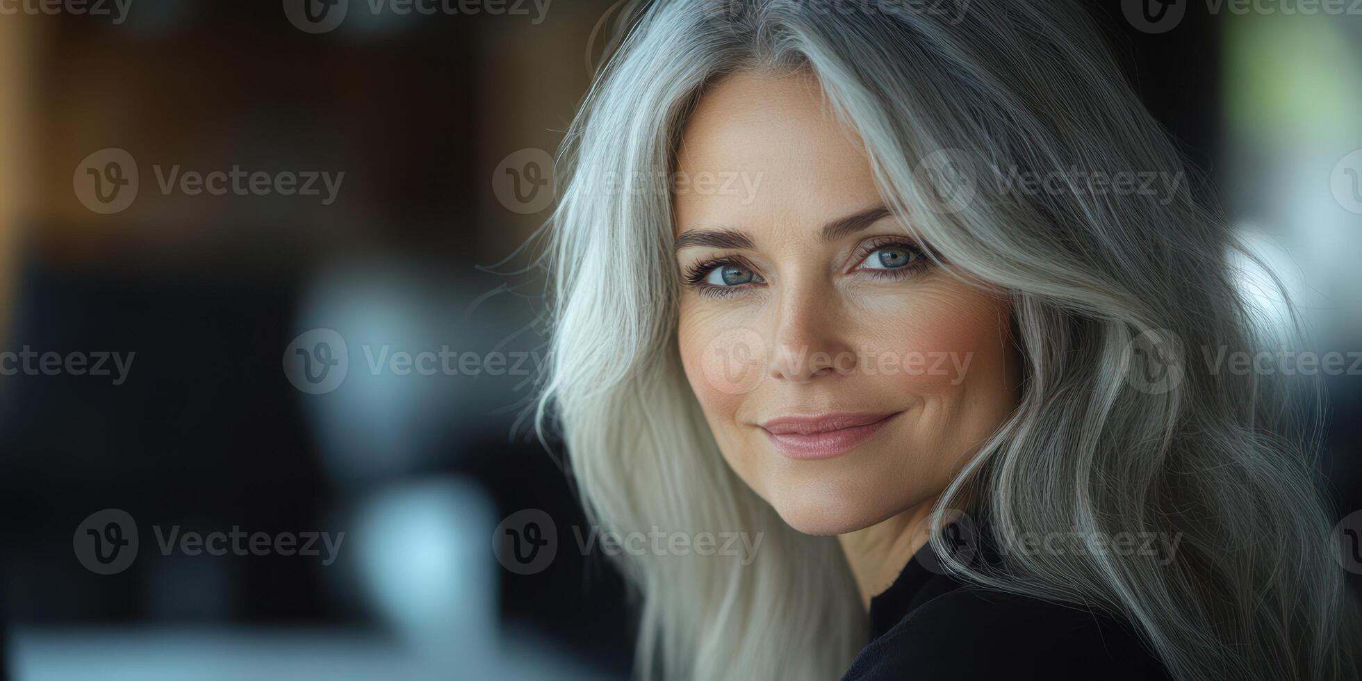 Mature woman with long silver hair smiling warmly in a relaxed indoor setting during daylight photo